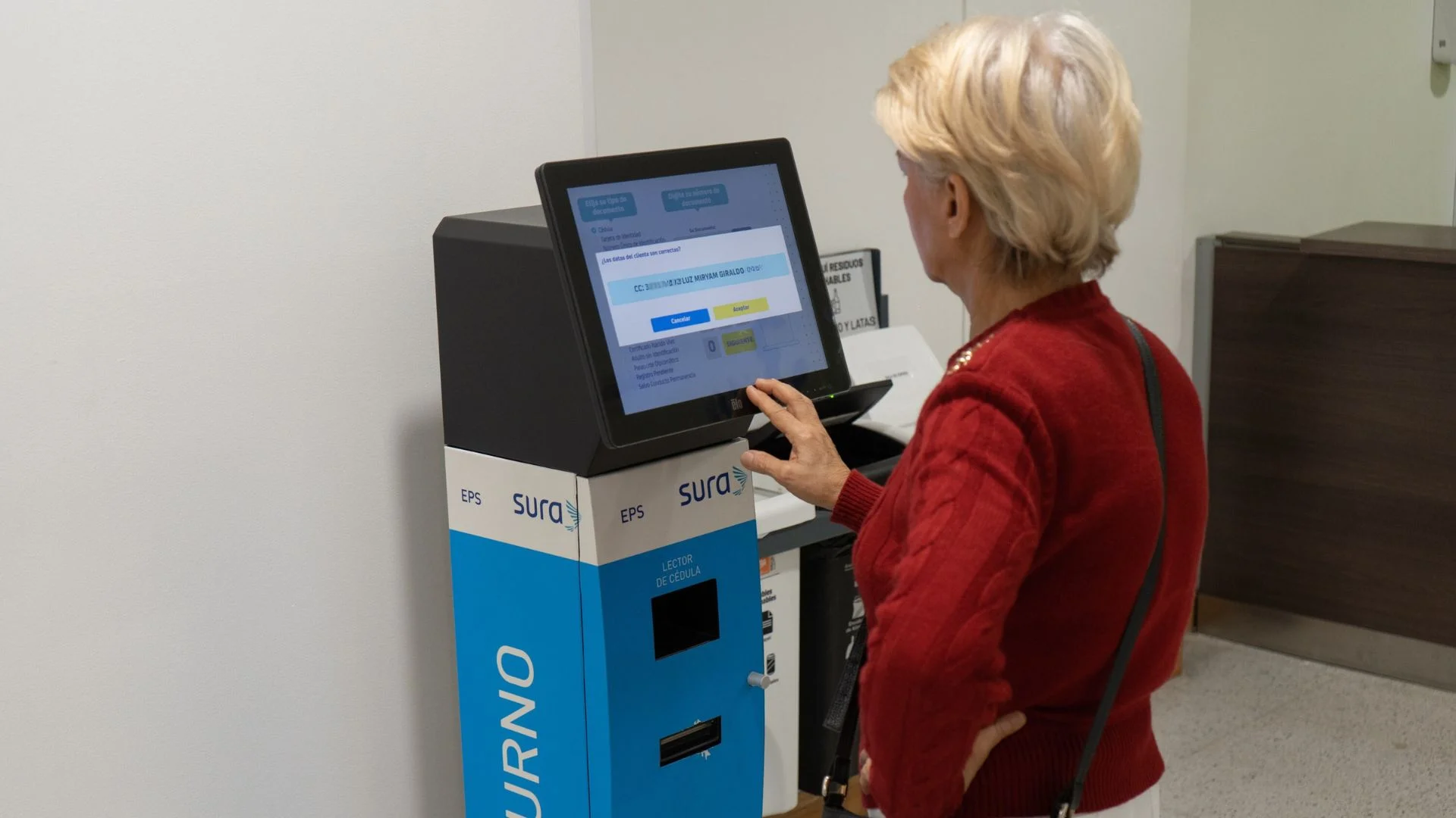 Mulher idosa solicitando sua senha em um totem touch de autoatendimento com leitor de documentos integrado